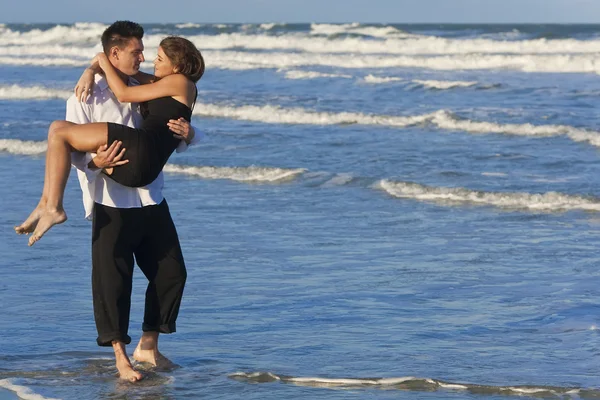 Uomo che trasporta donna in romantico abbraccio sulla spiaggia — Foto Stock