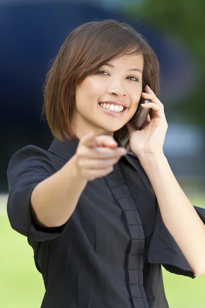 Mulher Oriental bonita em seu telefone celular inteligente e apontando — Fotografia de Stock