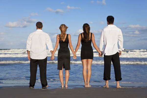 Quatro jovens, dois casais, de mãos dadas em uma praia — Fotografia de Stock