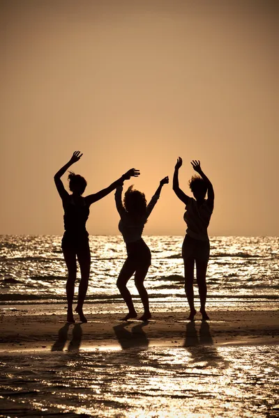 Tři mladé ženy tančí na pláži při západu slunce — Stock fotografie