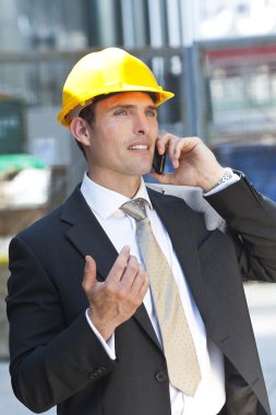 Man In Industrial Hard Hat and Talking On Cell Phone clipart