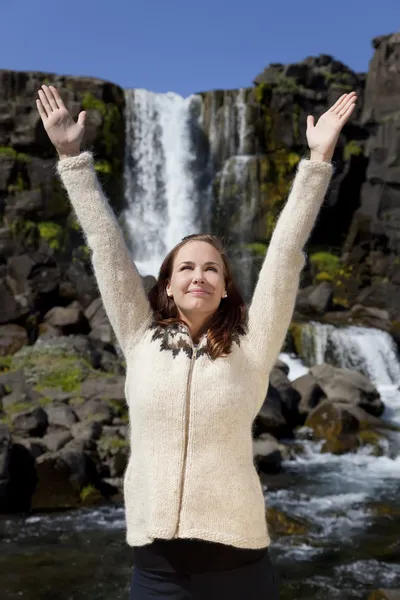 Красивая молодая женщина празднует поднятие рук у водопада — стоковое фото