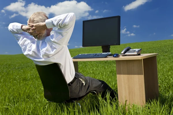Бизнесмен отдыхает за столом с компьютером в зеленом поле — стоковое фото