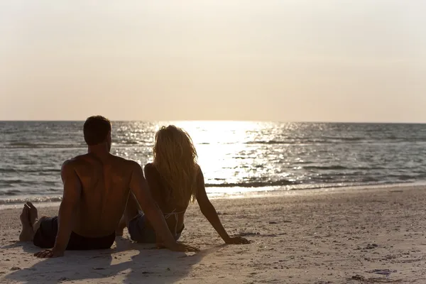 Młoda para mężczyzna i kobieta siedzi na plaży o zachodzie słońca — Zdjęcie stockowe