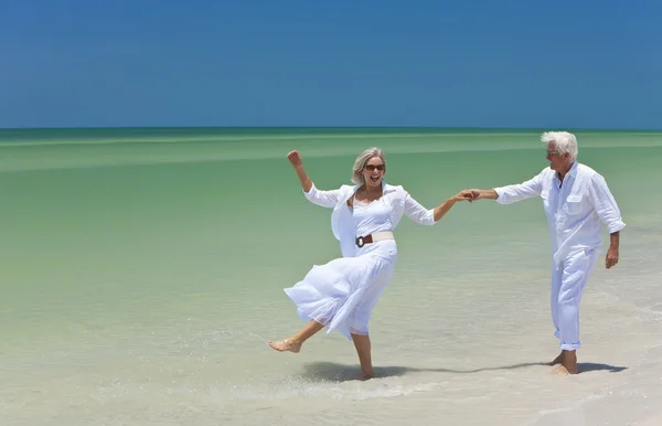 Feliz pareja mayor bailando sosteniendo las manos en una playa tropical —  Fotos de Stock