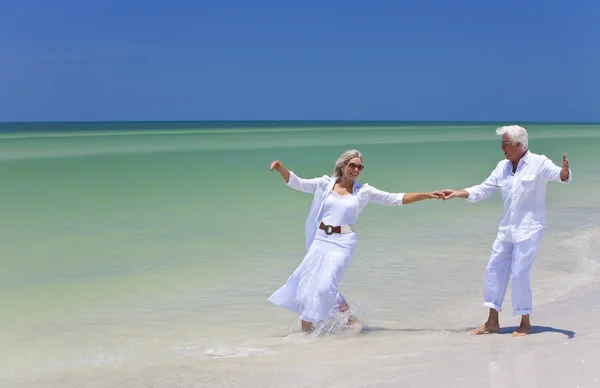 Felice coppia anziana che balla tenendo le mani su una spiaggia tropicale — Foto Stock