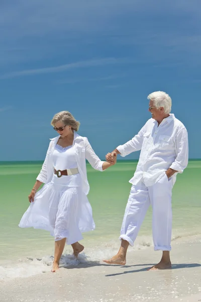 Счастливая пожилая пара гуляла, держась за руки на пляже — стоковое фото