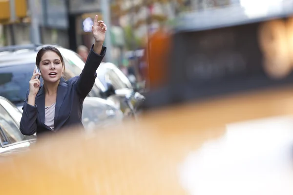 Νεαρή γυναίκα στο κινητό χαιρετώντας ένα κίτρινο ταξί — Φωτογραφία Αρχείου
