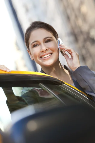 Młoda kobieta rozmowy na telefon komórkowy przez żółte taksówki — Zdjęcie stockowe