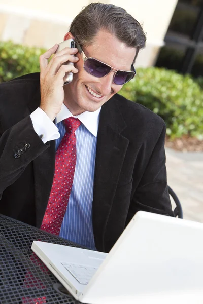 Επιχειρηματία σε γυαλιά ηλίου χρησιμοποιώντας φορητό υπολογιστή και κινητό τηλέφωνο — Φωτογραφία Αρχείου