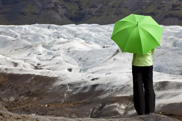 Milieu concept van een vrouw met groene paraplu door gletsjer — Stockfoto