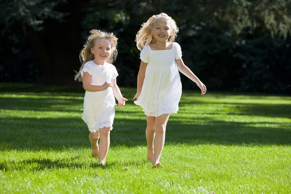Две симпатичные девушки бегают по зажженному солнцем зеленому парку — стоковое фото