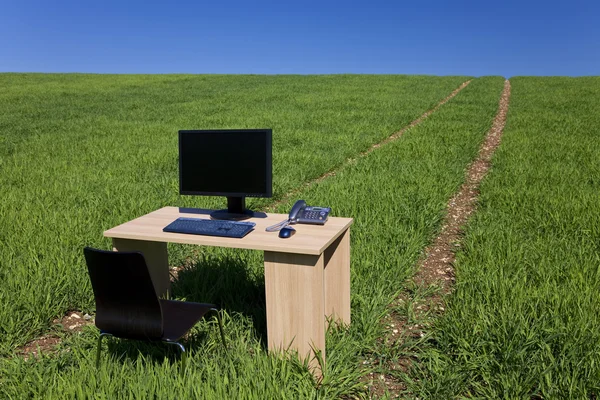 Bureau met telefoon en computer in groene veld met pad — Stockfoto