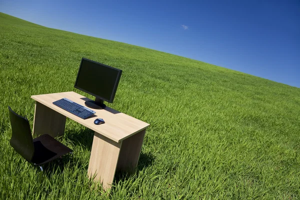 Bureau en de computer in groene veld met blauwe hemel — Stockfoto