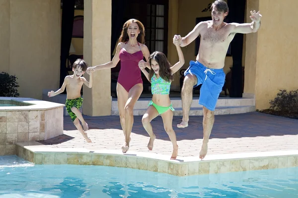 Família com duas crianças se divertindo saltando para a piscina — Fotografia de Stock