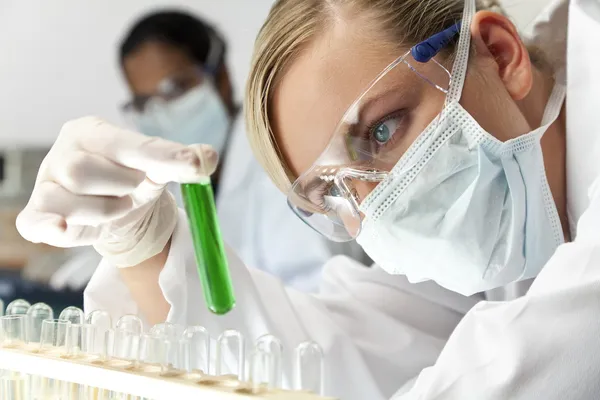 Vrouwelijke wetenschappelijke onderzoeksteam met groene oplossing in laborator — Stockfoto