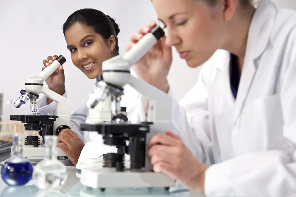 Vrouwelijke wetenschappelijke onderzoeksteam microscopen met een laborator — Stockfoto