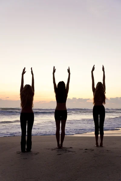 Üç kadın gündoğumu veya günbatımı Plajı Yoga uygulamak — Stok fotoğraf