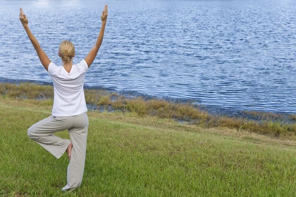 Hermosa joven practicando yoga junto a un tranquilo lago azul —  Fotos de Stock