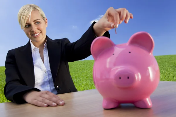 Frau steckt Münze in rosa Sparschwein auf der grünen Wiese — Stockfoto