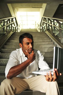 Indian Man with laptop sitting at the stair case clipart