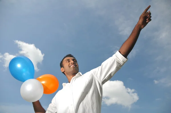 Індійський чоловік тримає різнокольорових кульок, вказуючи на відстані — стокове фото