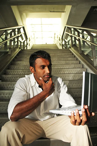 Homem indiano com laptop sentado na caixa da escada — Fotografia de Stock