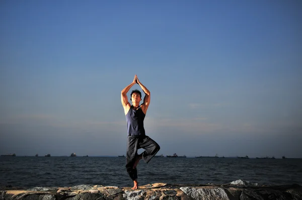 Asiatisk kinesisk man utövar yoga på stranden — Stockfoto