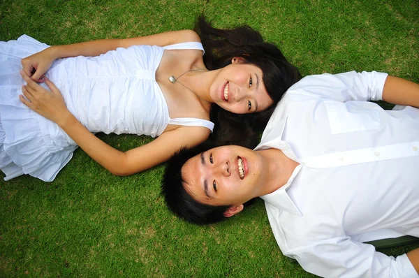Asiatiska kinesiska par liggande i gräset med olika uttryck — Stockfoto
