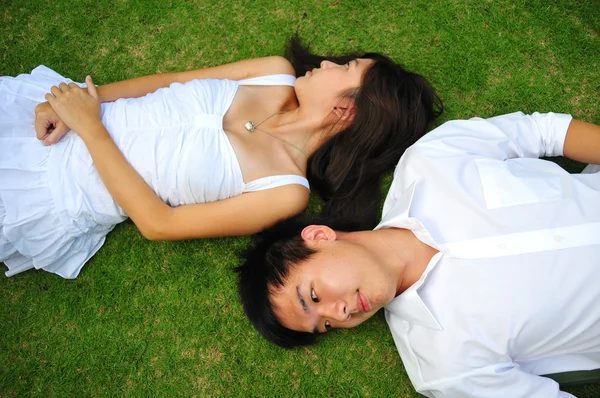 Asiatiska kinesiska par liggande i gräset med olika uttryck — Stockfoto