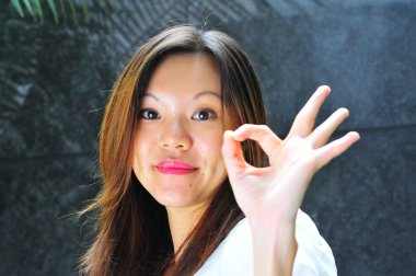 Smiling Asian chinese girl making an ok sign with her hands clipart