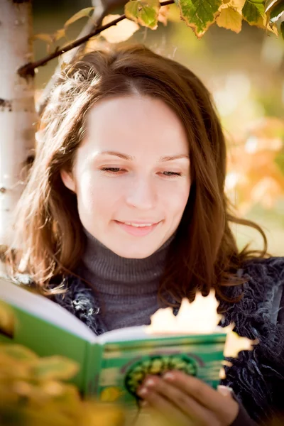 Mujer sonriente leyendo libro en otoño — Foto de Stock