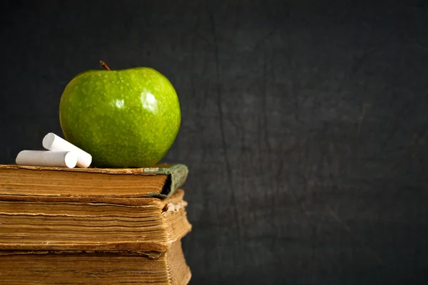 Мел и зеленое яблоко на старом учебнике — стоковое фото