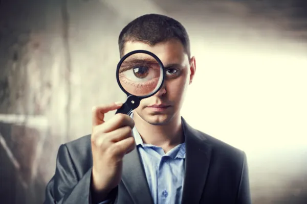 Detective looking through magnifying glass in subway tunnel. Lig — Stock Photo, Image
