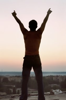 Freedom. Silhouette young man with lifted hands upwards clipart