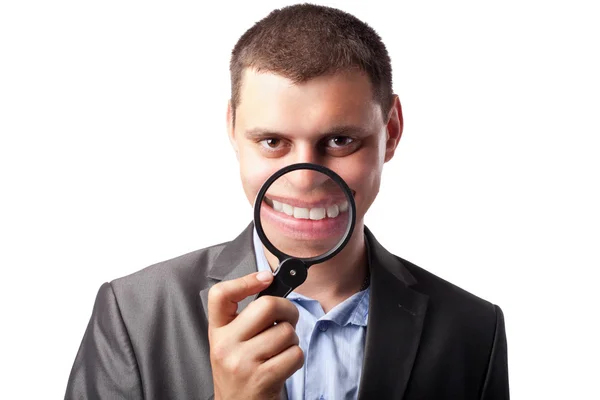 Hombre de negocios en traje sonriendo a través de lupa aislado en —  Fotos de Stock