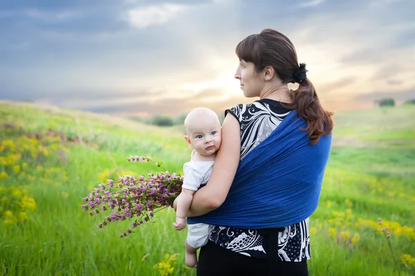 Mother and baby boy in sling on green meadow — Stock Photo, Image