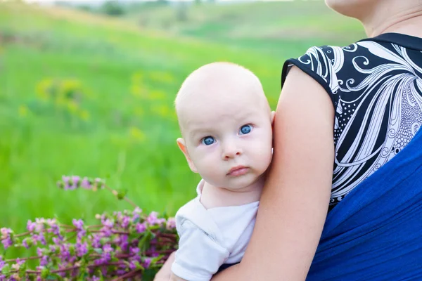 Мальчик на руках матери на зеленом лугу — стоковое фото