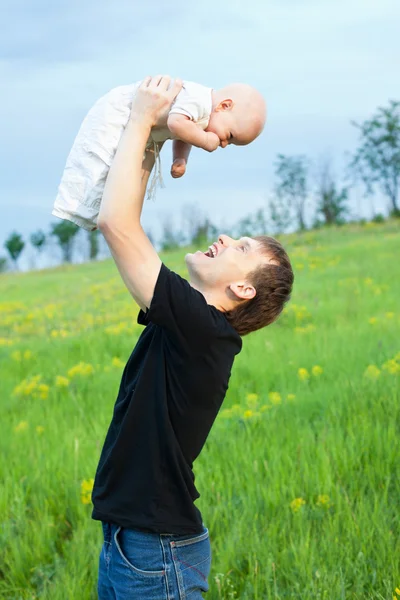 Jovem feliz jogando seu menino na natureza em declive — Fotografia de Stock