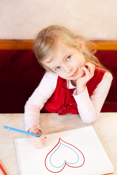 La niña sonriente dibuja el corazón en un álbum. Día de San Valentín —  Fotos de Stock