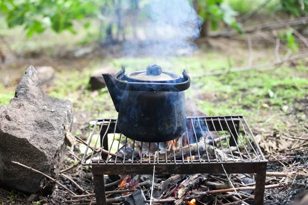 stock image Black old smoked teapot on the campfire on picnic in wood in the