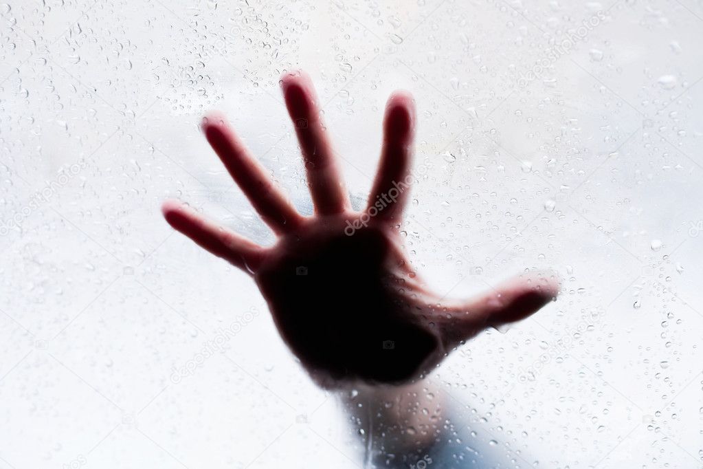 Silhouette of hand behind wet glass
