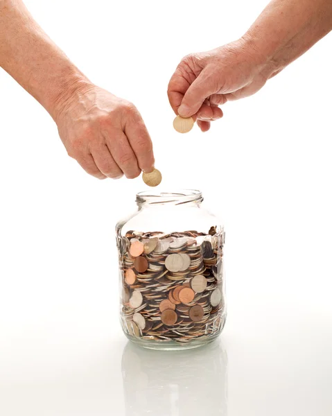 Старшие руки собирают монеты в стеклянную банку — стоковое фото
