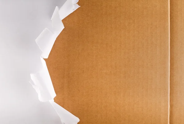 Papel de embalagem rasgado revelando caixa de papelão — Fotografia de Stock