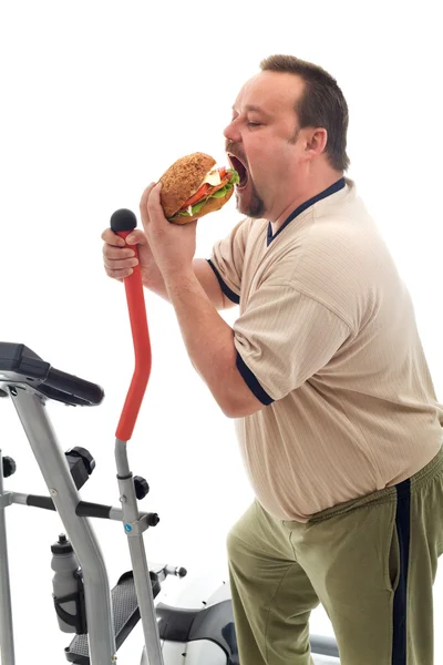 Man eating a large hamburger instead of working out — Stock Photo, Image