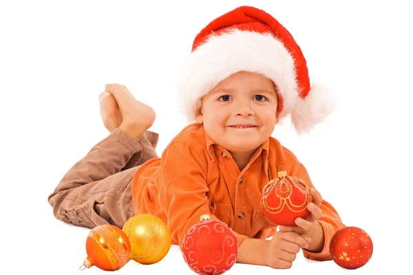 Junge mit Weihnachtsmütze liegt zwischen Christbaumkugeln - isoliert — Stockfoto