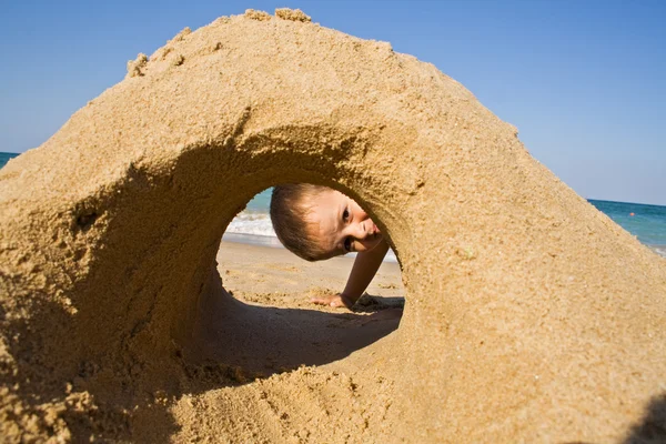 Pojken tittar genom ett sandslott på stranden — Stockfoto