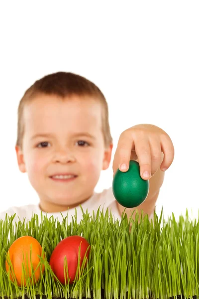 Junge legt bunte Ostereier ins Gras — Stockfoto