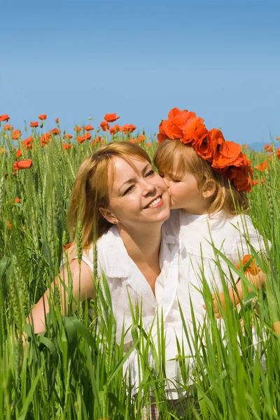 Kleines Mädchen küsst seine Mutter auf dem Mohnfeld — Stockfoto