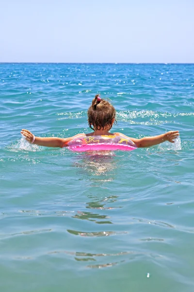 Маленькая девочка, плывущая в море розового колеса — стоковое фото